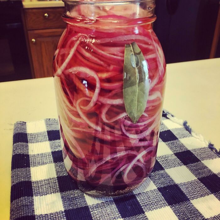 Jar of pickled red onions with a bay leaf on a checkered cloth, showcasing easy kitchen tricks for flavor enhancement.