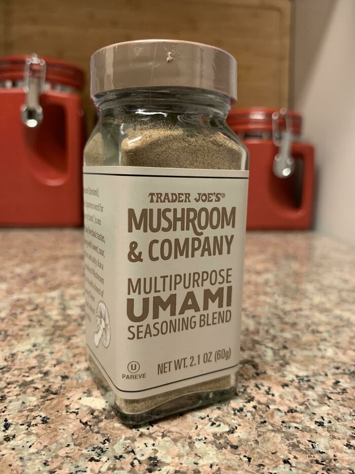 Trader Joe's mushroom and umami seasoning blend jar on kitchen counter with red canisters in background for kitchen tricks.