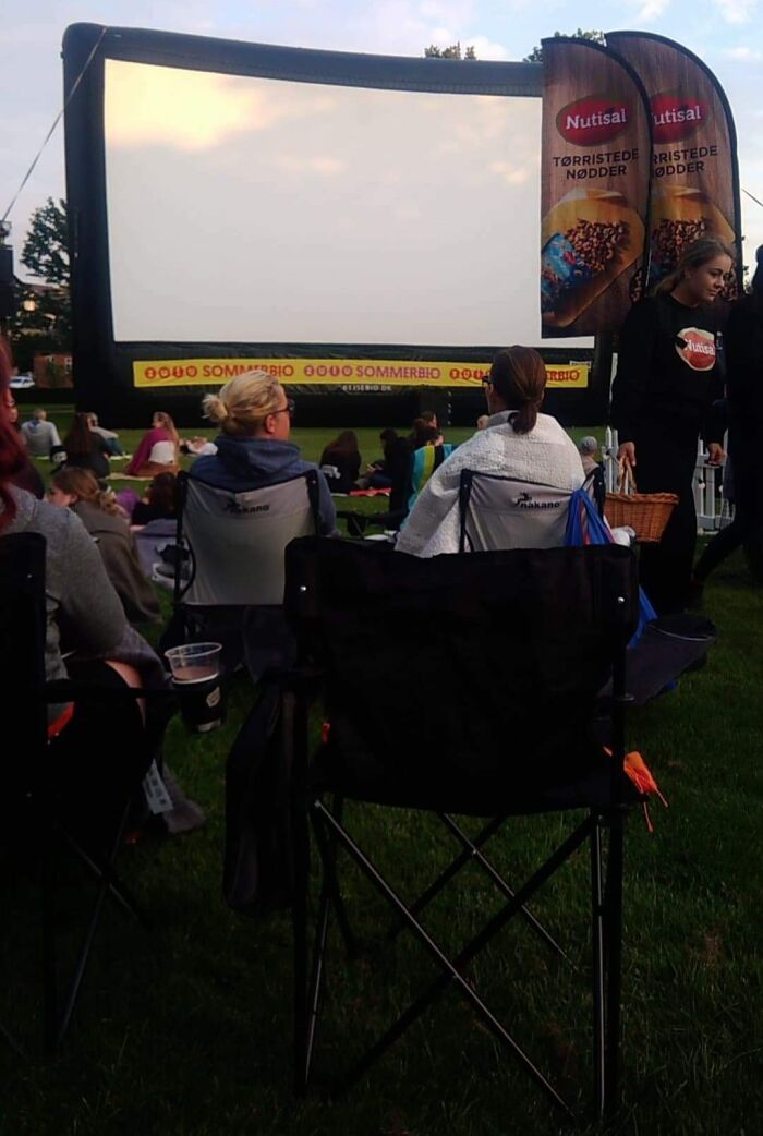 Outdoor movie screening in Denmark with people sitting on chairs and grass, enjoying a community event on a summer evening.
