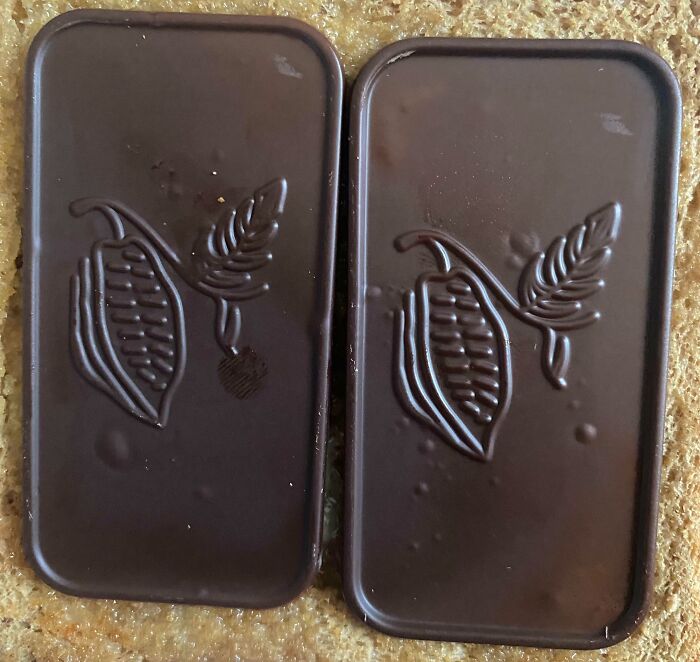 Two rectangular pieces of dark chocolate with cocoa pod designs on a textured surface, highlighting Danish prison cell simplicity.