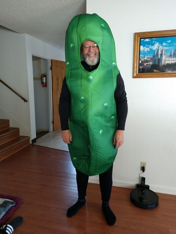 Man dressed in a funny pickle costume indoors, showcasing one of the funniest parents ever with a big smile.