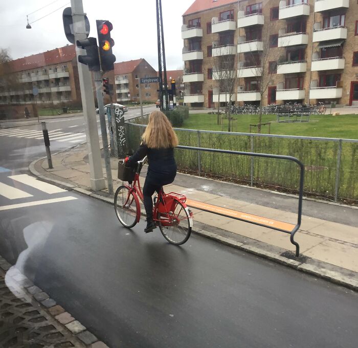 Woman riding a red bike on a wet street near apartment buildings in Denmark, illustrating Danish urban lifestyle and culture.