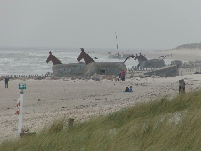 Concrete structures with horse sculptures on a Danish beach, showcasing unique Danish prison cell design and coastal scenery.