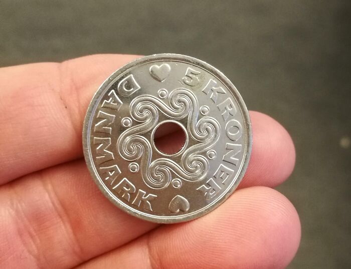 Hand holding a Danish 5 kroner coin featuring a hole in the center and decorative swirls, symbolizing Denmark.