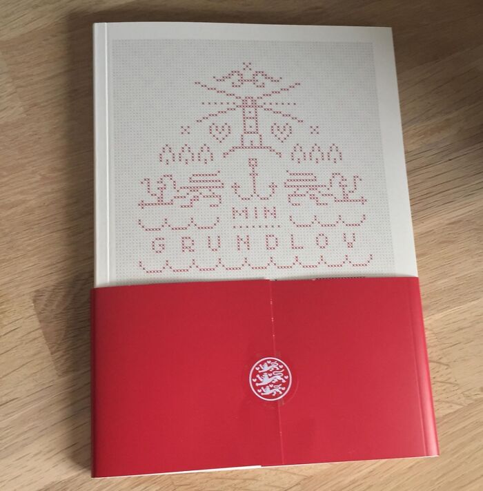 Book titled Min Grundlov with traditional Danish cross-stitch design and red band, representing Danish prison cell culture.