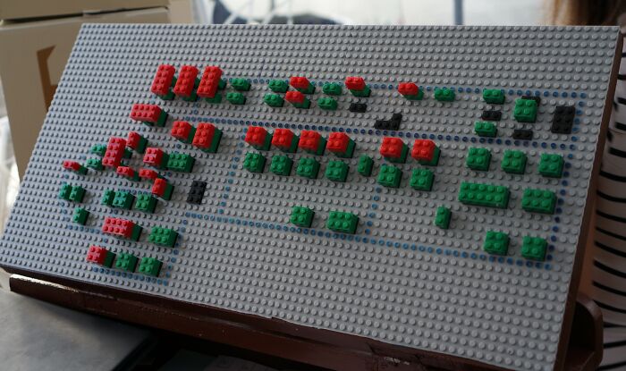 Model of a Danish prison cell layout made from red and green LEGO bricks on a grey baseplate.