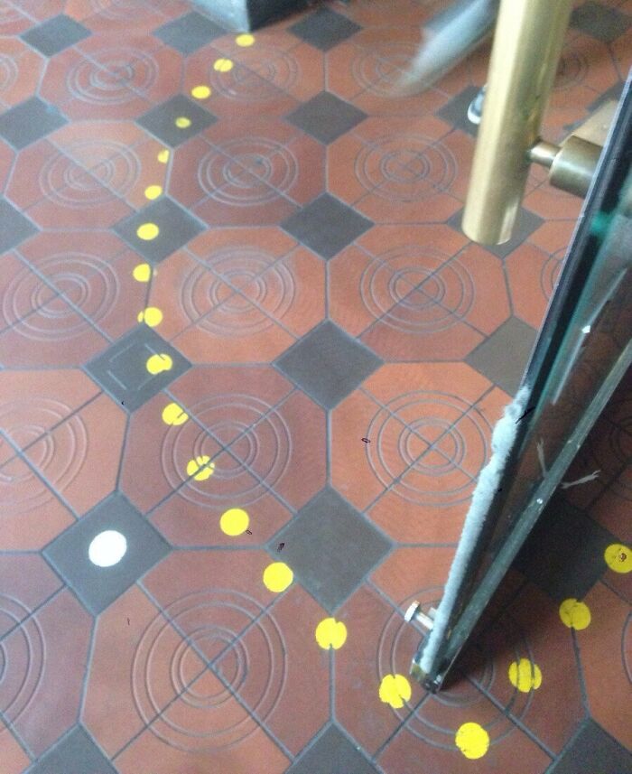 Close-up of a Danish prison cell floor with patterned tiles and yellow circular markings near a glass door handle.