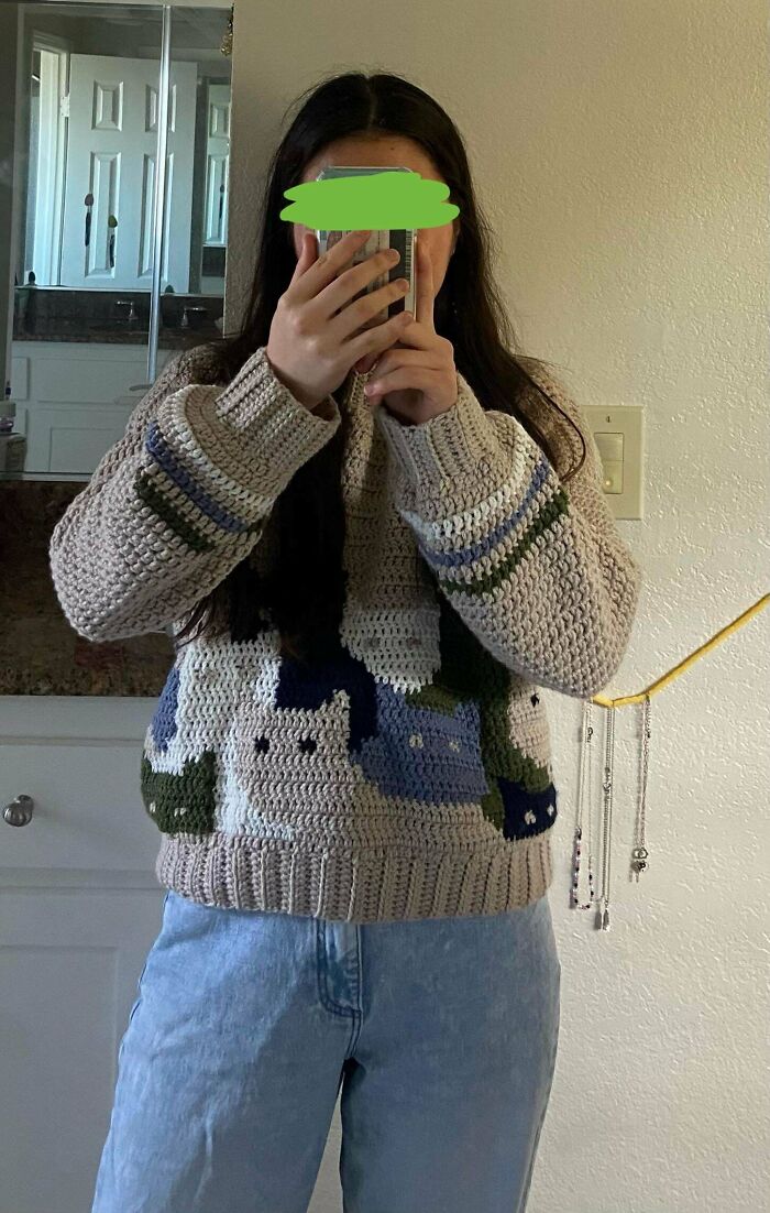 Person wearing a handmade crocheted sweater with cat patterns, showcasing a unique crocheting project.