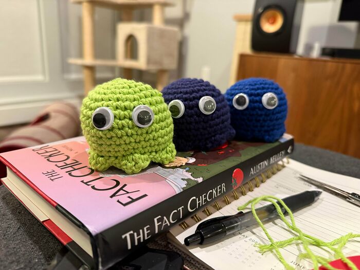 Three small crocheted octopus toys with googly eyes sit on top of a book and notebook in a cozy indoor setting.