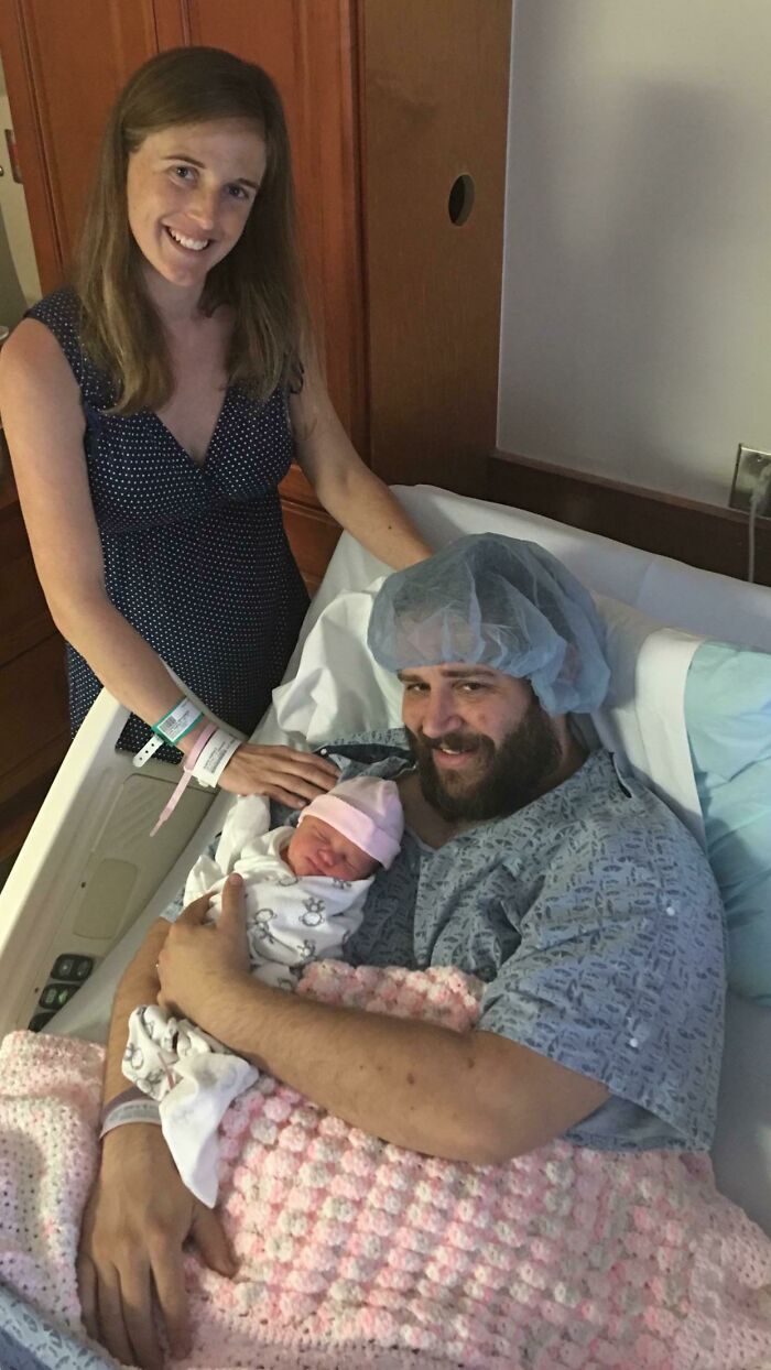 New parents smiling in hospital room holding newborn baby wrapped in blanket, capturing funniest parents moment.