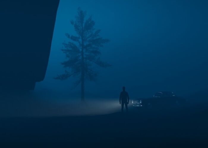 Silhouetted figure standing near a car at night in fog, evoking chaotic and eerie atmosphere of food delivery drivers.
