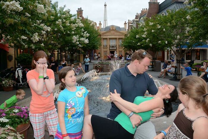 Family enjoying a playful moment by a fountain at an amusement park during a memorable trip with kids.