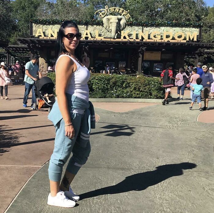 Woman posing for a photo at Disney's Animal Kingdom amusement park with visitors walking and exploring in the background.