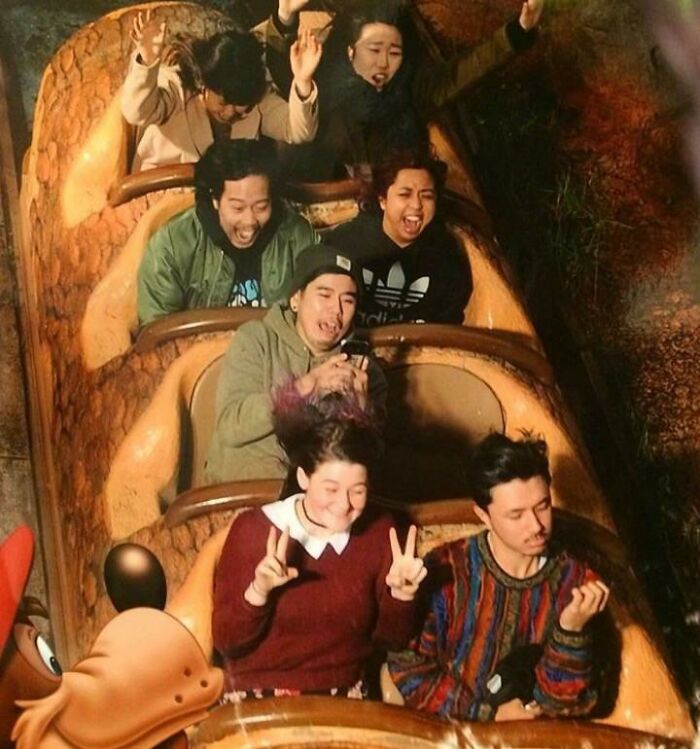 Group of people with varied reactions captured on a log ride in an amusement park photo souvenir.