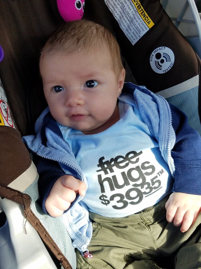 Baby wearing a humorous shirt with funny text, sitting in a car seat, showcasing one of the funniest parents' playful moments.