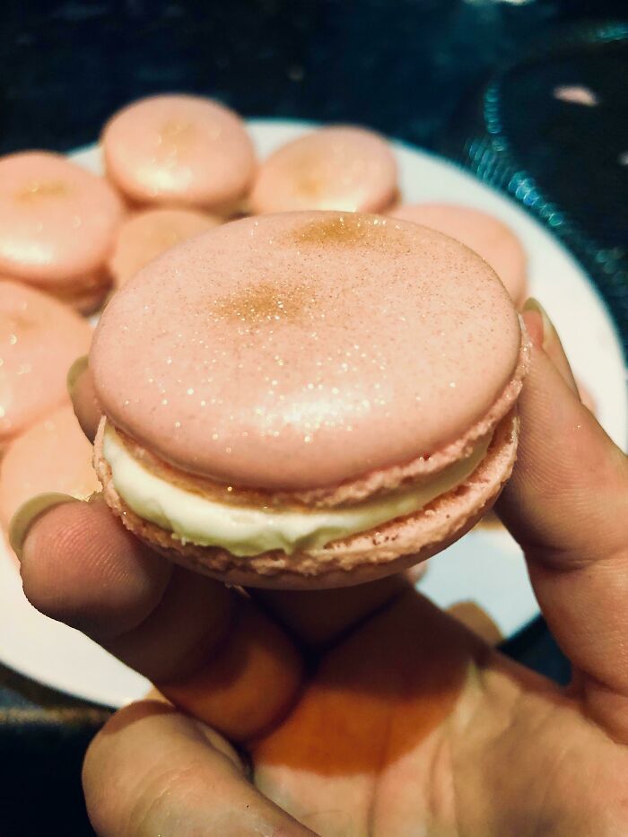 Close-up of a hand holding a pink macaron with cream filling, showcasing easy tricks to completely change your kitchen game.
