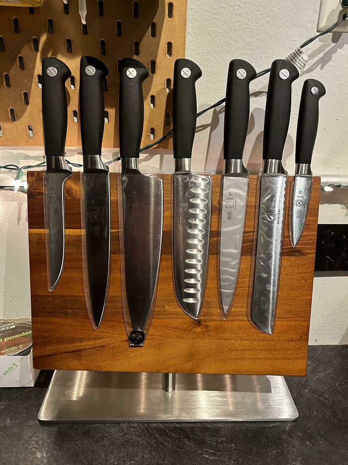 Set of kitchen knives with black handles neatly arranged on a wooden magnetic knife holder, showcasing easy kitchen tricks and tools.