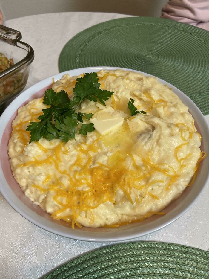 Creamy mashed potatoes topped with shredded cheese, butter, and fresh parsley on a table setting, kitchen tricks concept.