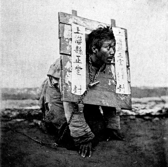 Man restrained in wooden stocks with chains, demonstrating shocking medieval history t*****e methods and devices.