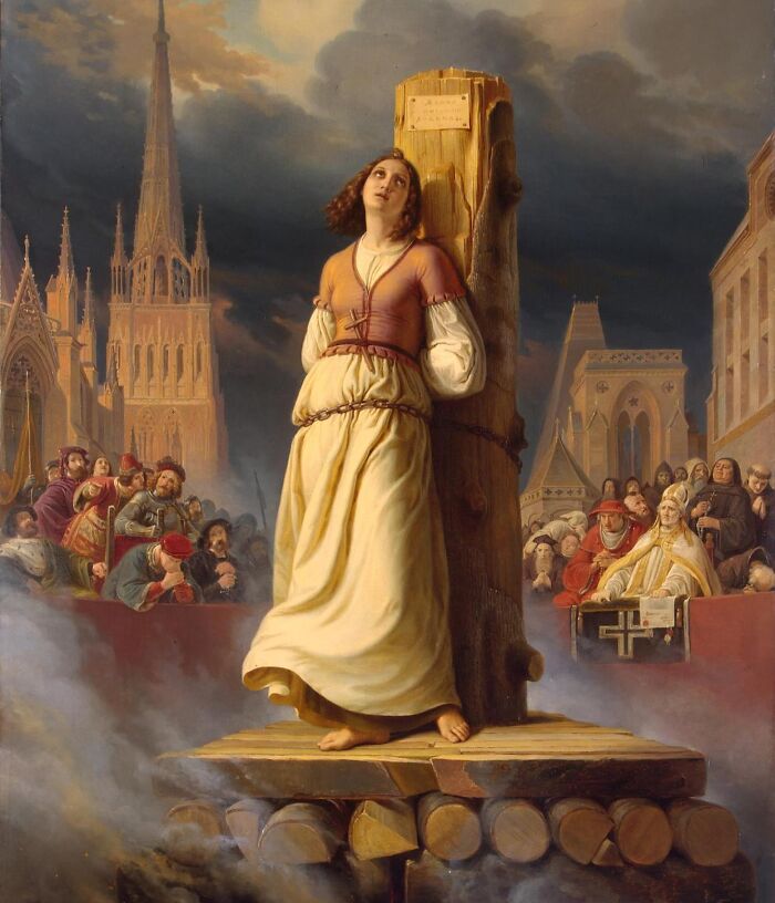 Medieval t*****e device with a woman tied to a wooden stake surrounded by a crowd in a historical setting.