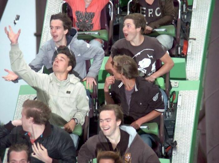 Group of young people with varied reactions on a roller coaster ride, a memorable amusement park photo moment.