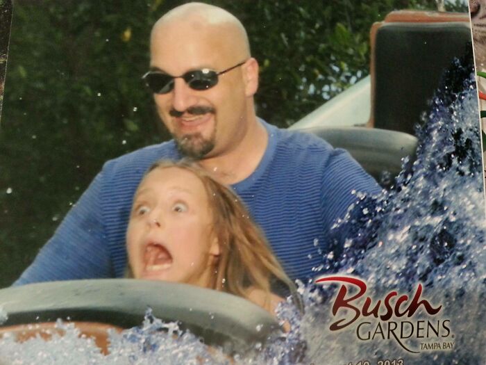 Man and young girl with excited expressions on water ride at amusement park creating memorable photos.