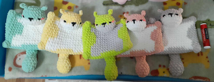 Five colorful crocheted animal plush toys with tails lined up next to a lip balm, showcasing crocheting projects.