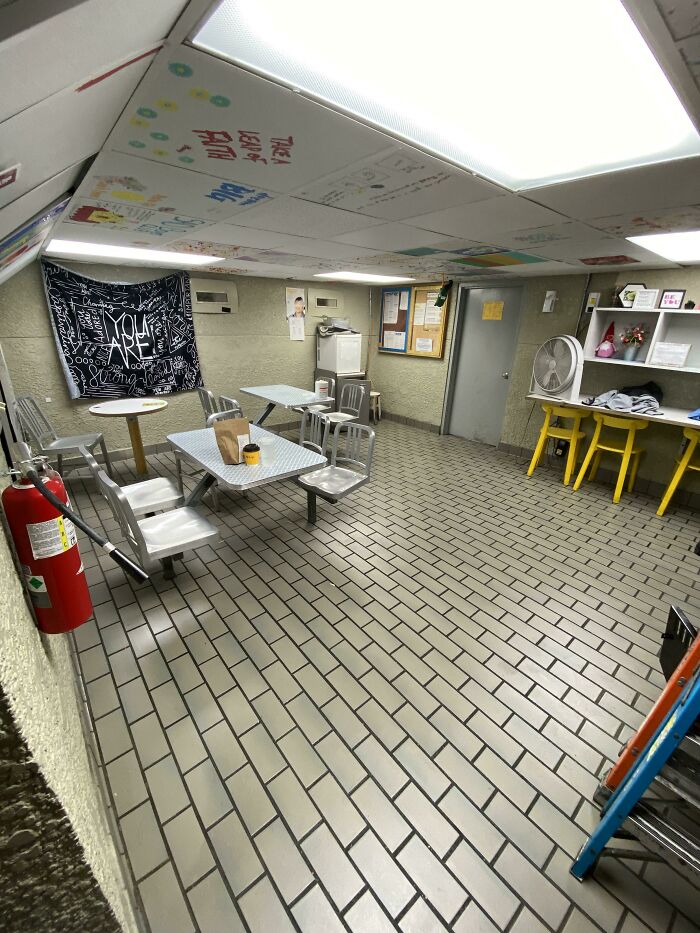 Break room with metal chairs and tables, tiled floor, fluorescent lights, and a prison-like atmosphere.