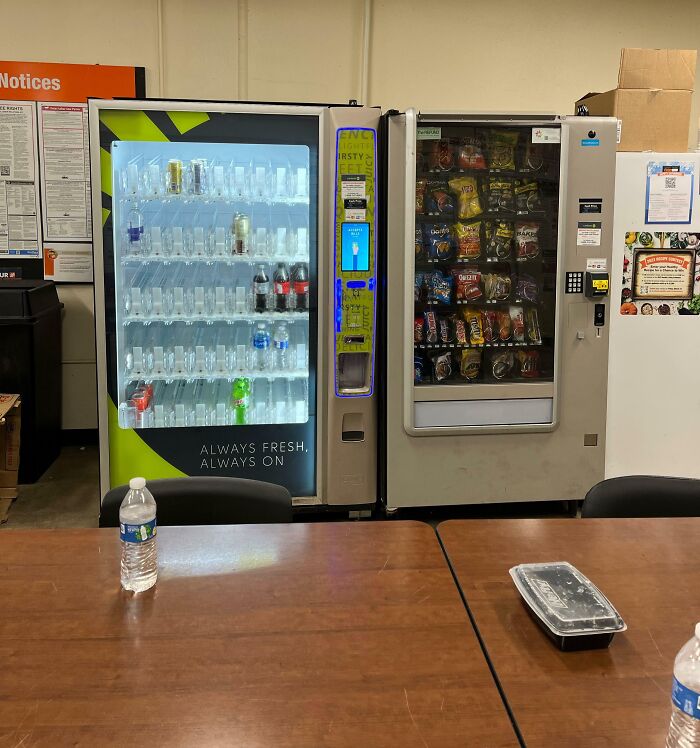 Break room with vending machines, empty snack slots, and basic seating, resembling one of the worst break rooms ever.