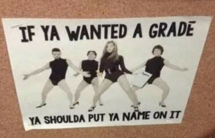 Funny teachers posing in black outfits with a humorous sign about grades, showcasing their sense of humor.
