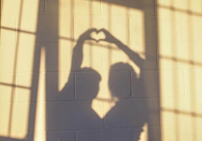 Shadow of two people forming a heart shape with their hands on a wall, symbolizing connection and shared moments.