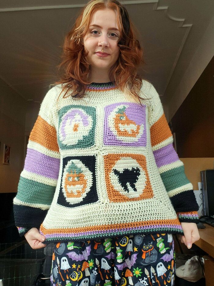 Young woman wearing a colorful crocheted sweater featuring Halloween-themed designs, showcasing crocheting skills and creativity.