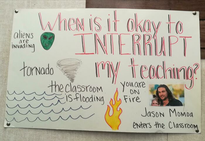 Funny teacher classroom sign with humorous reasons to interrupt teaching, including aliens, tornado, fire, and Jason Momoa entering.