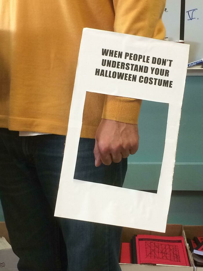 Person in casual clothes holding a humorous Halloween costume sign, showcasing funny teachers' sense of humor.