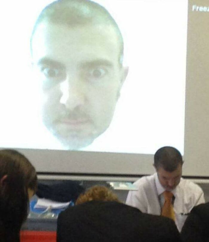 Teacher using a large projected face image to humorously engage students in a classroom setting.