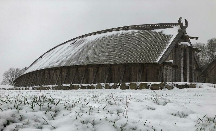 Traditional Danish wooden longhouse covered in snow, showcasing historic architecture in Denmark's winter landscape.