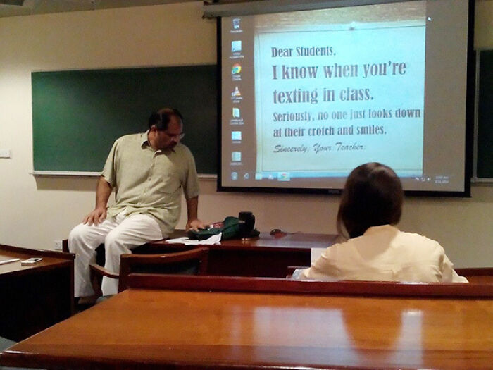 Teacher in classroom humorously warns students about texting in class on a projected screen, showing funny teachers with great sense of humor.