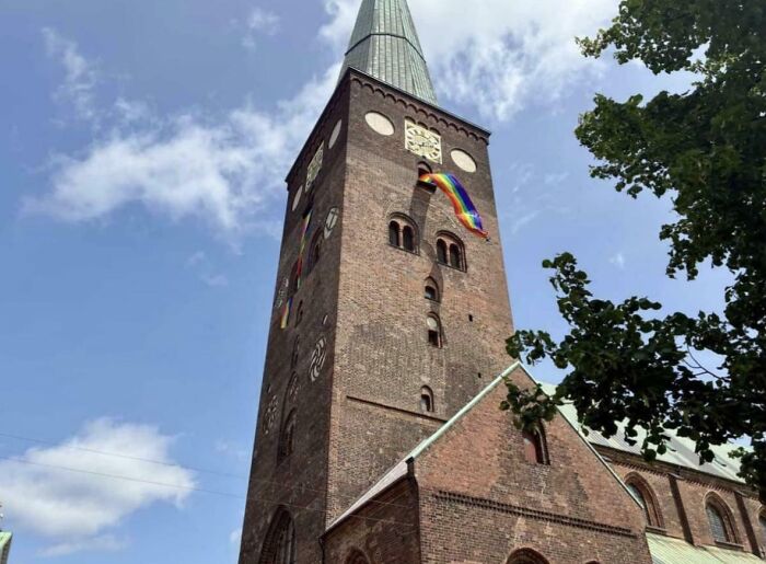 Historic Danish brick church tower under blue sky with colorful flags waving, showcasing unique Denmark architecture.
