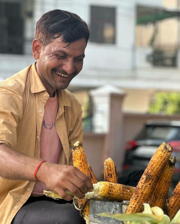 Smiling street vendor grilling corn on the cob, showcasing street photography that captures humanity in its purest form.