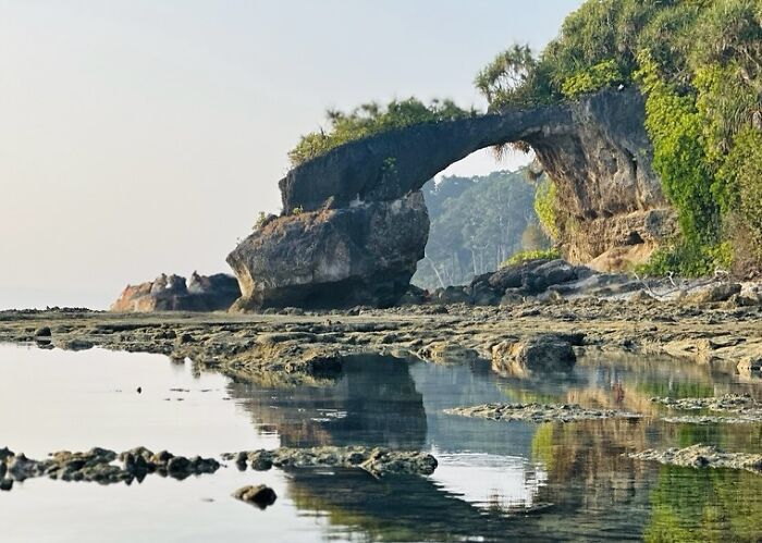 Natural rock arch formation by calm water, showcasing serene elements of street photography that captures humanity.
