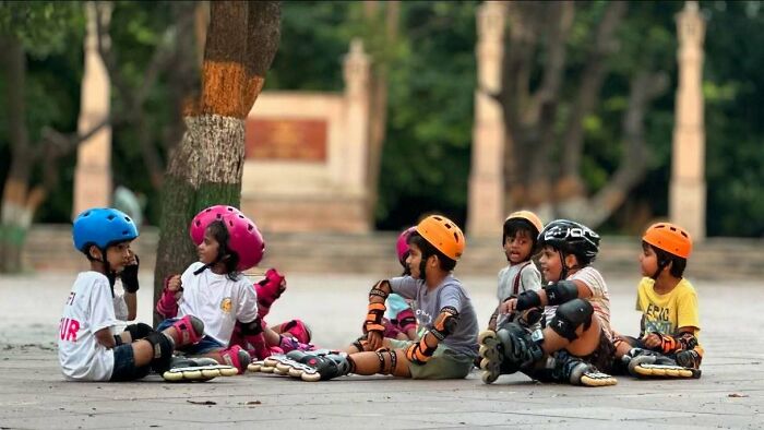 Children wearing helmets and protective gear sitting on pavement, captured in street photography that shows humanity.