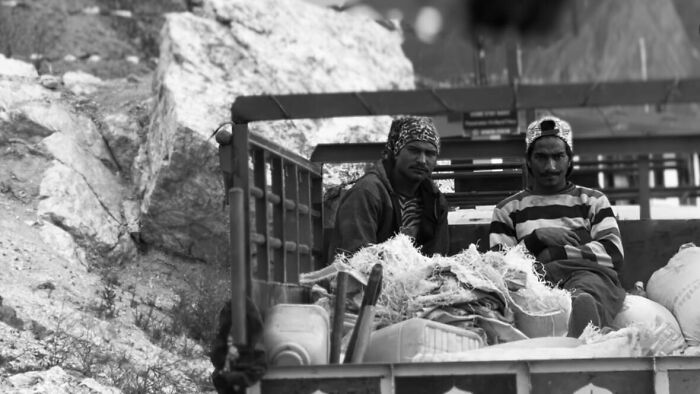 Two men sitting in the back of a truck surrounded by goods, captured in street photography showing humanity in its purest form.