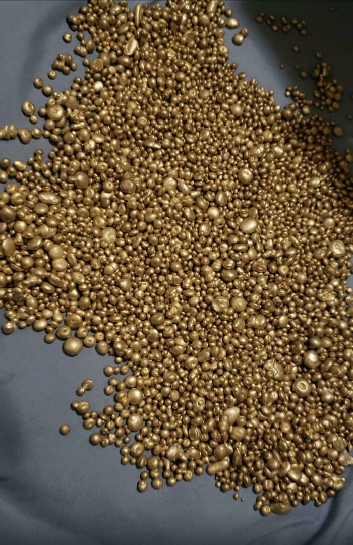 Close-up of curious things people discovered showing many small, shiny, gold-colored nuggets or beads on a dark surface.