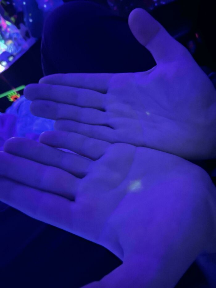 Hands glowing under blacklight revealing curious things people discovered in an unknown context with blue-purple light.