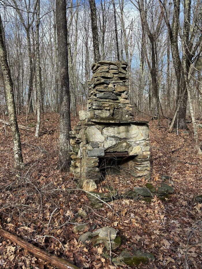 Old stone fireplace standing alone in a forest surrounded by fallen leaves, a curious thing people discovered outdoors.