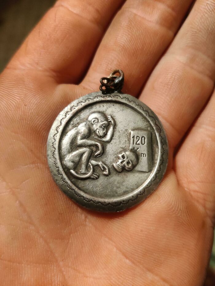 Hand holding a curious metal pendant featuring a monkey, skull, and 120 km marker, one of the curious things people discovered.