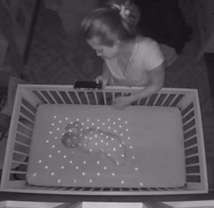 Woman using a phone projecting dots on a baby sleeping in a crib, illustrating curious things people discovered.
