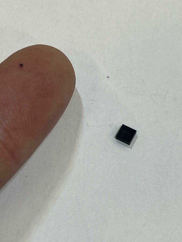 Close-up of a tiny black square object next to a fingertip showing size in curious things people discovered.