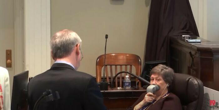 Man using a mysterious medical device to breathe while seated in a courtroom setting, curious things discovered.