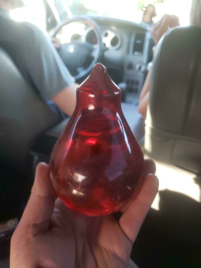 Hand holding a mysterious red translucent object inside a car, one of 46 curious things people discovered with no idea what they were.